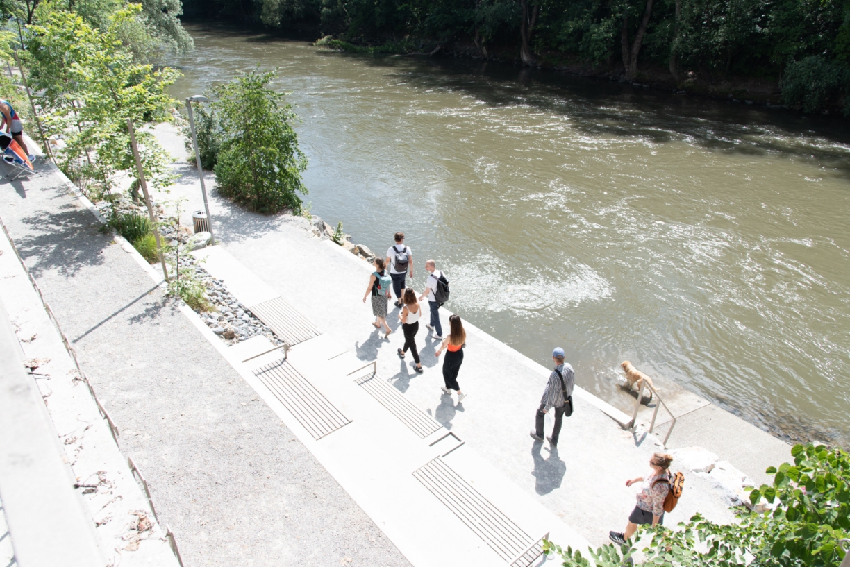 Menschen gehen am befestigten Flussufer entlang