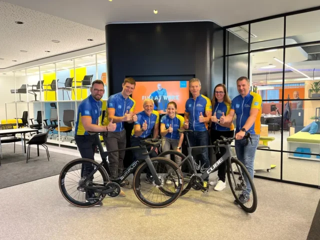 Mitarbeiter:innen von hali stehen mit eigenem Dress hinter zwei Fahrrädern und posieren mit ausgestrecktem Daumen