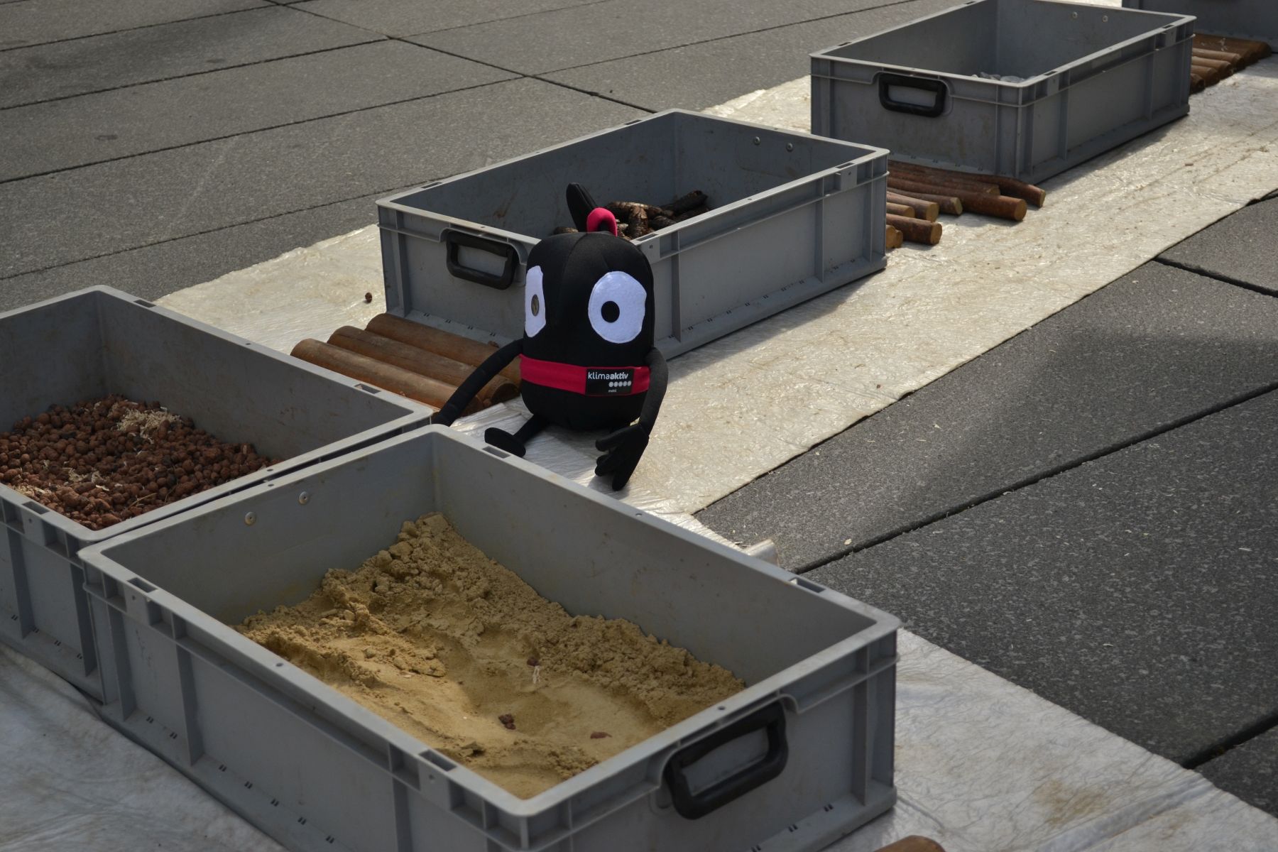 Plastik-Kisten mit verschiedenen Materialien wie Sand, Bockerl, Kies usw. werden am Boden entlang aufgebaut