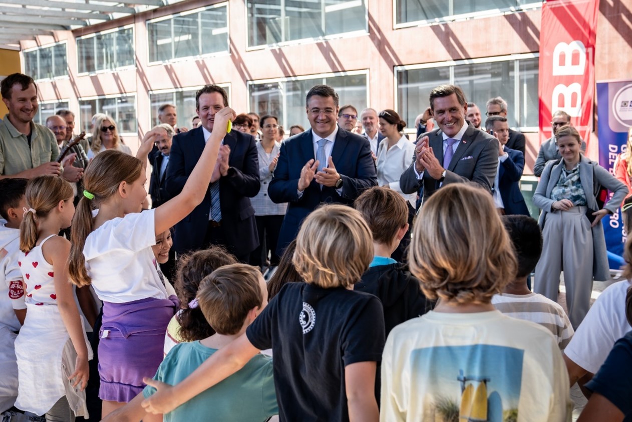 Am Bahnhof umringt von Kindern stehen der EU-Kommissar Apostolos Tzitzikostas zu Besuch am Innsbrucker Bahnhof (mitte), neben dem Bundesminister Peter Hanke (rechts) und Landesrat René Zumtobel (links). (2025)