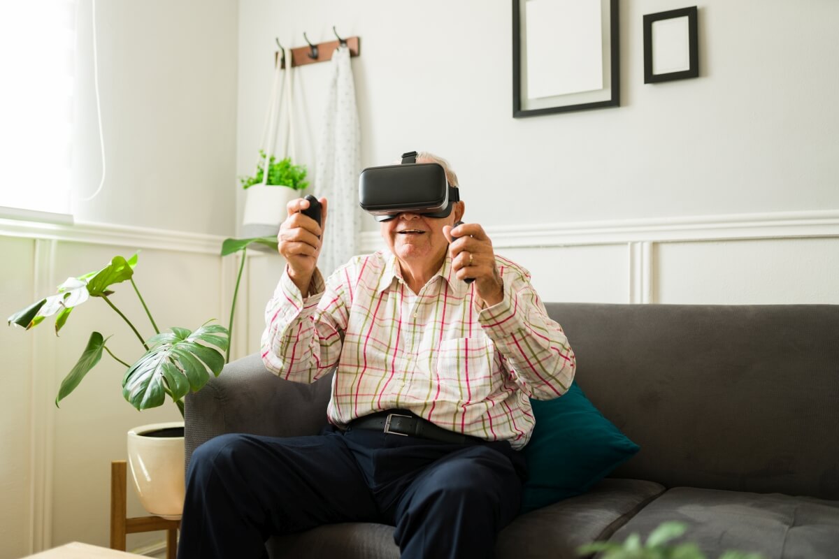 Älterer Herr sitzt auf der Couch und bedient ein VR-Headset